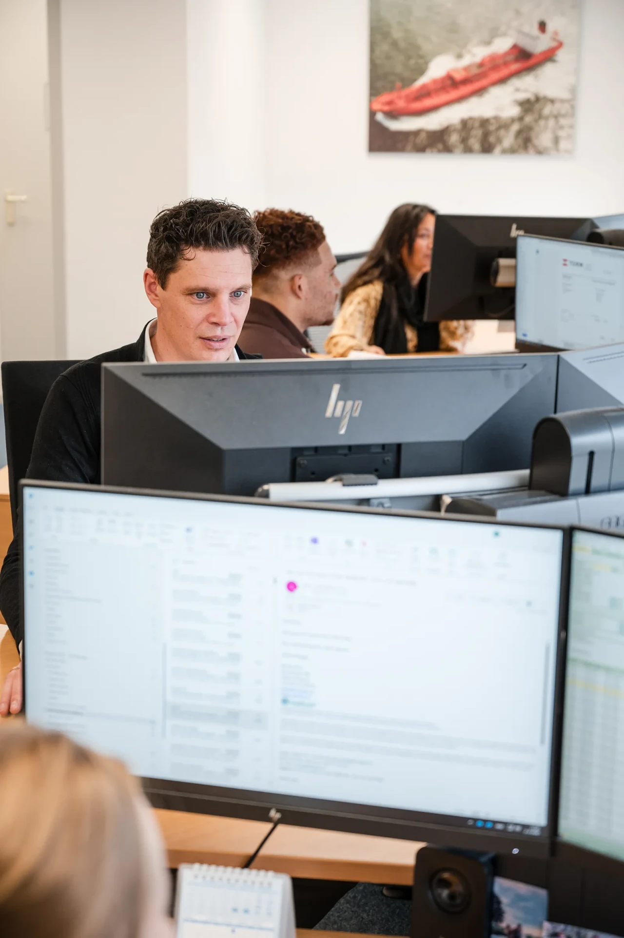Imatech employees work at multiple monitors in a shared office, focusing on service and administrative tasks at their desks.
